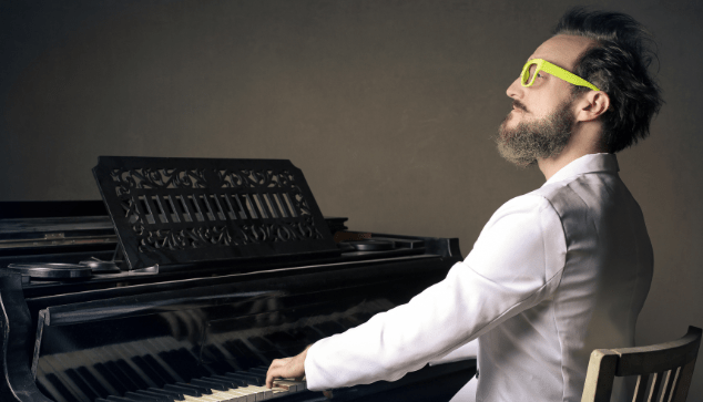 man in bright yellow glasses playing a grand piano
